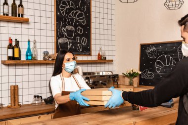 Tıbbi maskeli bir kafe sahibi masanın yanındaki kuryeye kutu veriyor. 