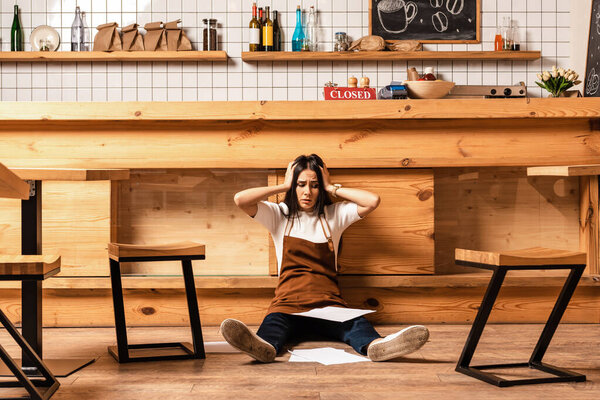 Stressed cafe owner with closed eyes and papers near table and chairs on floor
