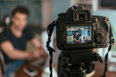 Dijital kameraya bakarken dizüstü bilgisayar kullanan genç vlogger 'ın seçici odağı 