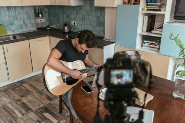 Mutfakta dijital kameranın yanında gitar çalan genç vlogger 'ın yüksek açılı görüntüsü
