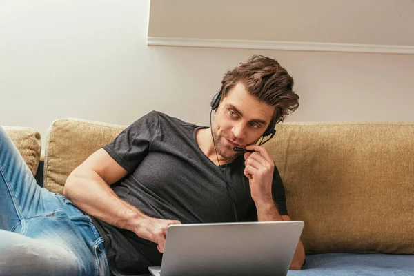 Szkeptikus Férfi Fülhallgató Feküdt Kanapén Közel Laptop Miközben Otthon Dolgozik — Stock Fotó