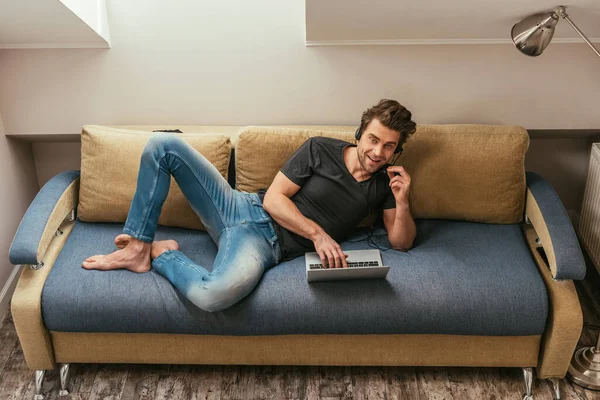 High Angle View Smiling Man Headset Lying Sofa Laptop Looking — Stock Photo, Image