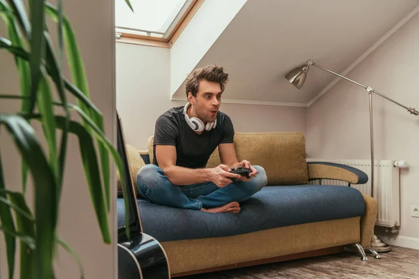 Kyiv Ukraine エイプリル社2019 ソファに座っている間 首の再生ビデオゲームでワイヤレスヘッドフォンで興奮した男の選択的焦点 — ストック写真
