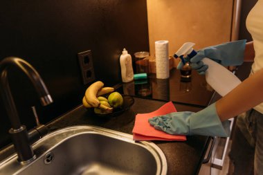 Kırpılmış plastik eldivenli kadın karantina sırasında lavaboyu bez ve antiseptik spreyle temizliyor.