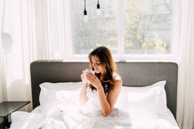 çekici pozitif kız sabahları kendini izole ederken yatakta kahve içiyor.