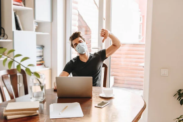 Giovane Maschera Medica Mostrando Pollice Verso Basso Vicino Laptop Tazza — Foto Stock