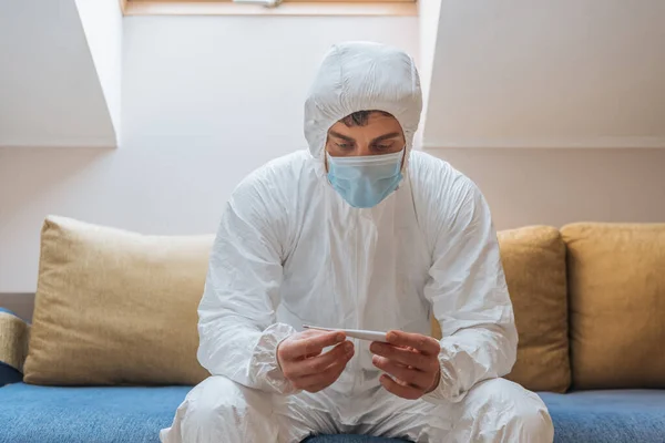 Junger Mann Schutzanzug Und Schutzmaske Sitzt Auf Sofa Und Schaut — Stockfoto