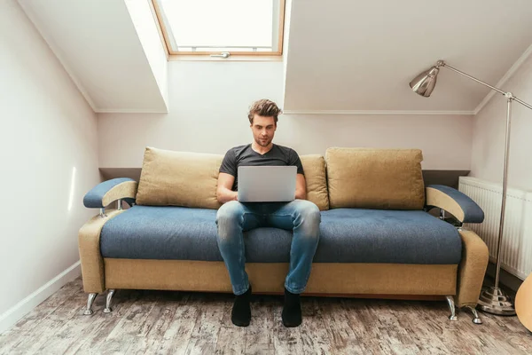 Handsome Attentive Young Man Using Laptop While Sitting Sofa Attic — Stock Photo, Image
