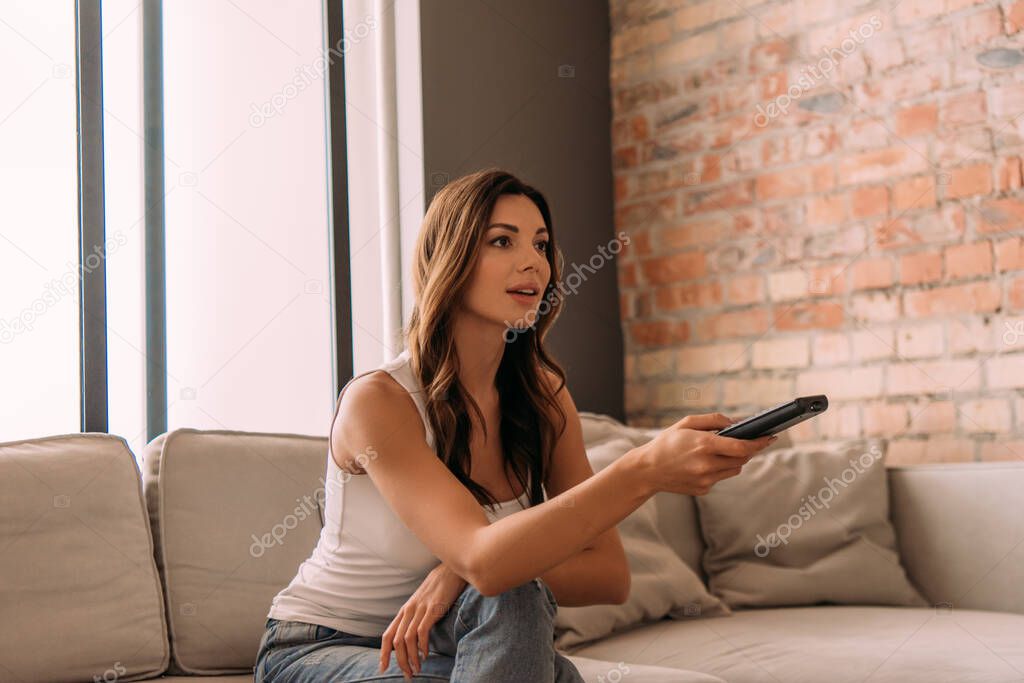 attractive woman holding remote controller and watching tv during self isolation 