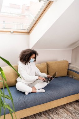 Laptop kullanarak tıbbi maskeli Afrikalı Amerikalı serbest çalışanların seçici odak noktası 