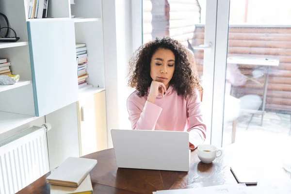 Freelancer Afroamericano Mirando Ordenador Portátil Cerca Teléfono Inteligente Libros Taza —  Fotos de Stock