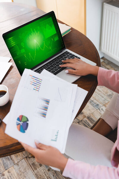 cropped view of african american freelancer holding documents near laptop with business analysis 