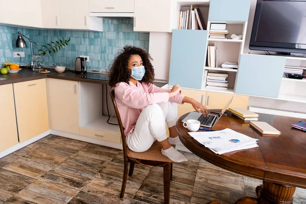 African American Freelancer Medical Mask Sitting Laptop Cup Charts Graphs — Stock Photo, Image