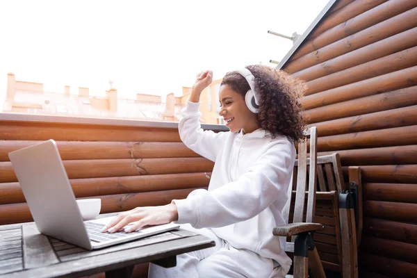 Alegre Afroamericano Freelancer Auriculares Inalámbricos Escuchando Música Cerca Portátil Taza —  Fotos de Stock