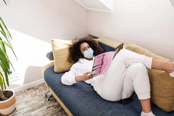 Young African American Woman Medical Mask Lying Sofa Reading Magazine — Stock Photo, Image