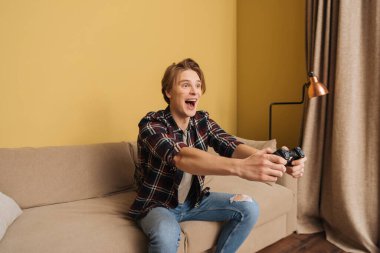 KYIV, UKRAINE - 24 Nisan 2020: oturma odasında video oyunu oynarken elinde joystick tutan mutlu adam 