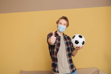 Medikal maskeli adam elinde futbol topu tutuyor ve parmağını kaldırıyor. Karantina sona erdi.