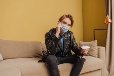 Medikal maskeli, ceketli, elinde biletler olan şık bir adam akıllı telefondan konuşuyor, karantina konseptinin sonu. 