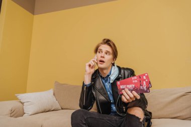 Medikal maskeli ve ceketli şık bir adam elinde gece partisi biletleri ve akıllı telefondan konuşma, karantina konseptinin sonu. 