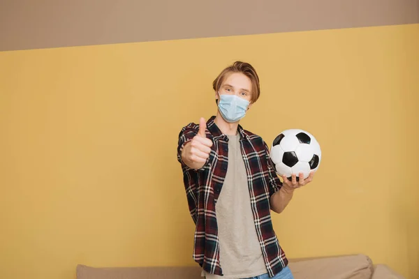 Άνθρωπος Ιατρική Μάσκα Κρατώντας Ποδόσφαιρο Και Δείχνοντας Τον Αντίχειρα Επάνω — Φωτογραφία Αρχείου