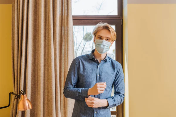 Νεαρός Άνδρας Ιατρική Μάσκα Κοιτάζοντας Την Κάμερα Στο Σπίτι — Φωτογραφία Αρχείου