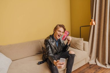 Medikal maskeli ve ceketli mutlu adam gece parti biletleri tutuyor ve selfie çekiyor, karantina konseptinin sonu. 