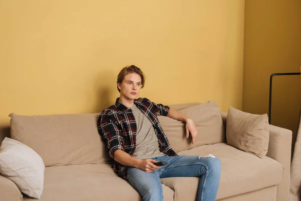 ハンサムな男はリモコンを持ってソファに座って隔離の概念を終わらせ — ストック写真