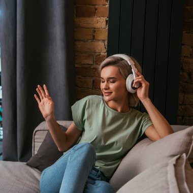 Kablosuz kulaklıkla müzik dinlerken el kol hareketi yapan kapalı gözlü çekici bir kadın.