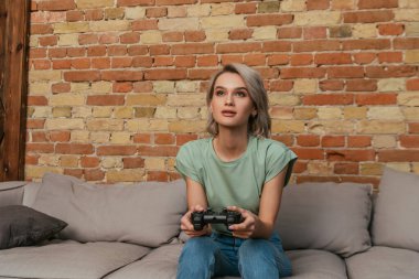 KYIV, UKRAINE - 30 Nisan 2020: evde joystick ile video oyunu oynayan odaklı genç kadın