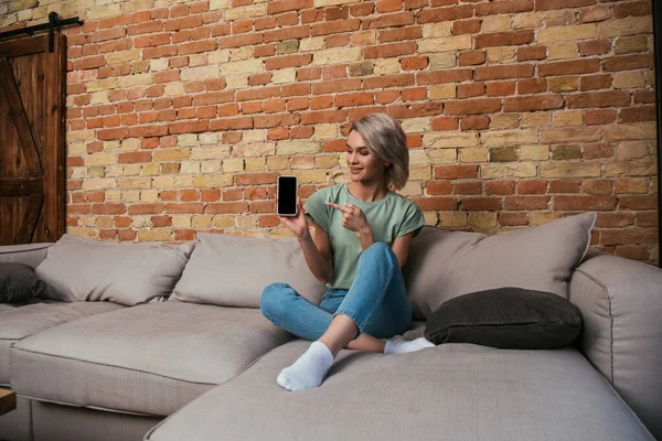 Atractiva Joven Sentada Sofá Apuntando Con Dedo Teléfono Inteligente Con — Foto de Stock