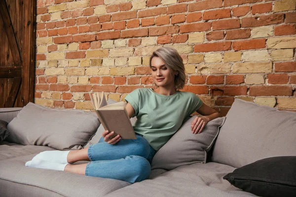 Bella Donna Sorridente Seduta Sul Divano Vicino Muro Mattoni Libro — Foto Stock