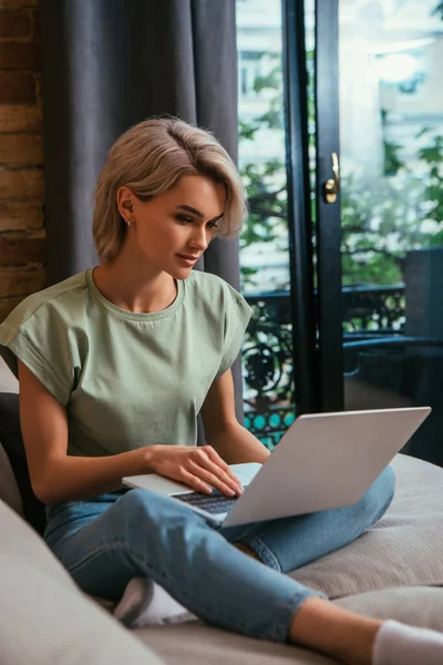 Fokuserad Ung Kvinna Sitter Soffan Nära Fönstret Och Använder Laptop — Stockfoto