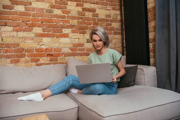 Bonita Jovem Mulher Usando Laptop Enquanto Sentado Sofá Perto Parede — Fotografia de Stock