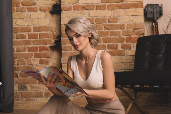 attractive young woman reading magazine while sitting on floor at home