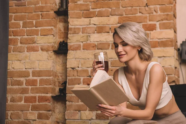 Χαμογελαστή Γυναίκα Κρατώντας Ένα Ποτήρι Κόκκινο Κρασί Ενώ Διαβάζοντας Βιβλίο — Φωτογραφία Αρχείου