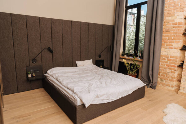 spacious bedroom with large bed, dark curtains on window and potted plants on windowsill