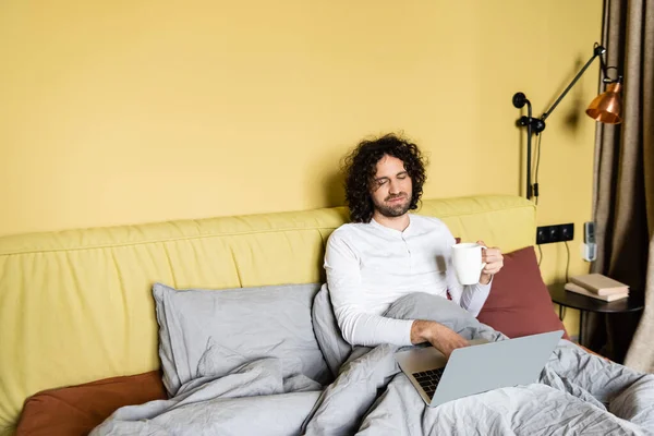 Serious Freelancer Using Laptop While Holding Cup Coffee Bed — Stock Photo, Image