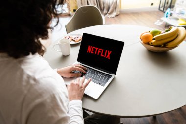 KYIV, UKRAINE - 25 Nisan 2020: Netflix web sitesi ile birlikte meyve, kahve fincanı ve tost tabağı kullanan serbest çalışanın arka görünümü