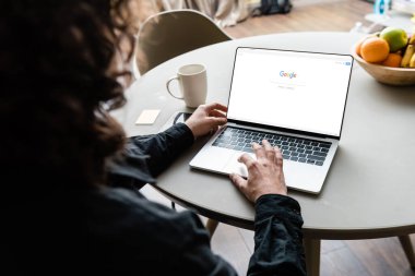 KYIV, UKRAINE - 25 Nisan 2020: Google 'ın kahve fincanı, yapışkan notlar ve meyvelerin yanında ekranda Google kullanarak serbest çalışanın arka görünümü