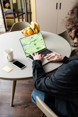 Akıllı telefon, kahve fincanı, yapışkan notlar ve meyvelerin yanında haritalı dizüstü bilgisayar kullanan serbest çalışanın arka planı