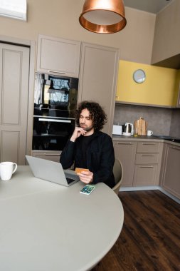KYIV, UKRAINE - 25 Nisan 2020: ekranda anasayfalı Apple akıllı telefonuna bakarken kredi kartı tutan düşünceli serbest yazar