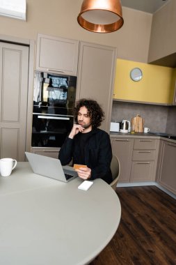 Bilgisayarın yanında kredi kartı tutan ciddi bir serbest çalışan, boş ekranlı akıllı telefon ve kahve fincanı.
