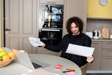 KYIV, UKRAINE - 25 Nisan 2020: Dizüstü bilgisayar, youtube uygulamalı akıllı telefon ve mutfak masasında kredi kartı tutan kafası karışık tele-işçinin seçici odak noktası 