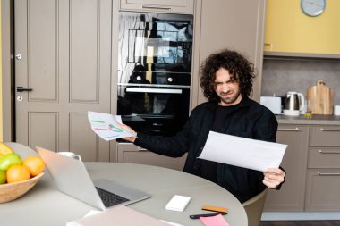 Kafası karışık serbest çalışanın, mutfak aletlerinin, kredi kartlarının ve meyvelerin yanında kağıt tutmasının seçici odak noktası 