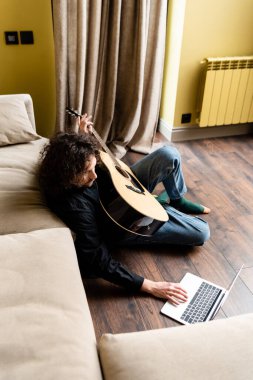 Evdeki Webinar sırasında elinde akustik gitar tutan ve dizüstü bilgisayar kullanan adamın genel görünümü 