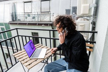 Akıllı telefondan konuşan kıvırcık adam, balkonda web alışveriş sitesi var. 