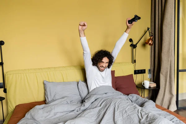Kyiv Ukraine エイプリル社2020年25日 ベッドでビデオゲームをしながら勝者のジェスチャーを示す幸せな若者 — ストック写真
