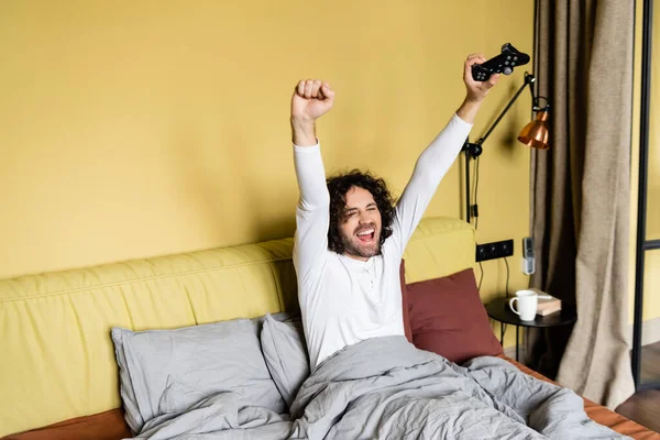 Kyiv Ukraine エイプリル社2020年25日 ベッドでビデオゲームをしながら勝者のジェスチャーを示す興奮した若者 — ストック写真