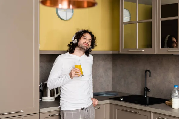 Glimlachende Man Draadloze Koptelefoon Die Wegkijkt Terwijl Hij Sinaasappelsap Vasthoudt — Stockfoto