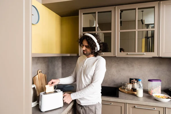 Krullende Man Draadloze Hoofdtelefoon Zetten Brood Broodrooster Tijdens Het Bereiden — Stockfoto